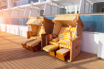 Roofed wicker beach chairs on the deck of a cruise ship.