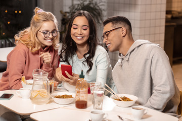 Asian girl showing photos with her boyfriend to two her friends.