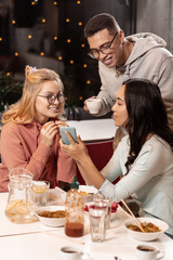 Asian woman showing friends dress that she liking while the guy drinking coffee next to her.
