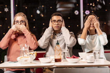 Friends sitting in restaurant and doing scene about three wise monkeys.