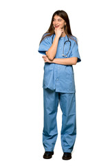 Full-length shot of Young nurse looking to the side with the hand on the chin on isolated white background