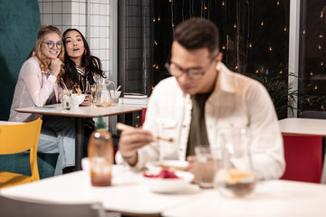 Two students trying to attract the attention of eating guy.