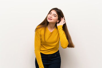 Young woman with yellow sweater listening to something by putting hand on the ear