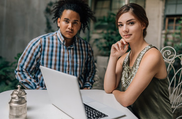 Portrait of two young creative business people looking into the camera. Sitting in a outside alfresco bistro. Working from a cafe with laptop