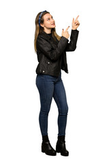 A full-length shot of a Teenager girl with leather jacket pointing with the index finger and looking up on isolated white background