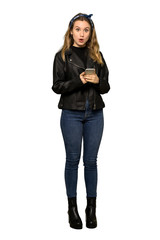 A full-length shot of a Teenager girl with leather jacket sending a message with the mobile on isolated white background