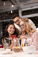 Girl seeing familiar face while watching photo on the phone of her female friend which she showing.