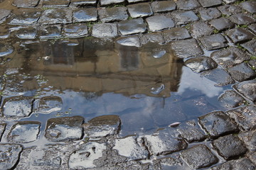 Palazzo riflesso nell'acqua di una pozza durante la pioggia in un vicolo di Roma con sanpietrini come sfondo