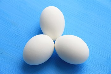 Three white eggs in the shell are on a blue wooden background