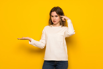 Teenager girl over yellow wall making the gesture of madness putting finger on the head