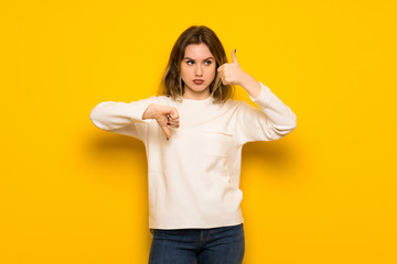 Teenager girl over yellow wall making good-bad sign. Undecided between yes or not