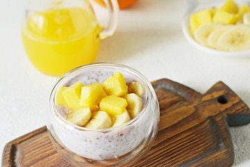 Chia pudding with mango pulp  in beautiful glasses with green mint leaves and cut fresh ripe tropical fruit, orange juice for breakfast on a light background - raw vegetarian sweet organic dessert. 