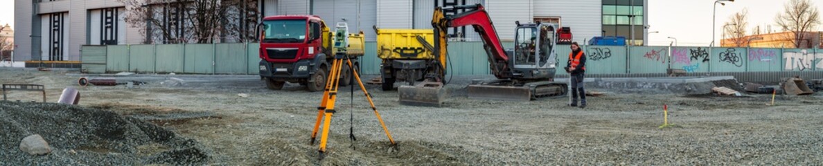 Panoramic view of surveyor engineer with equipment (theodolit or total positioning station) on the construction site of the road with construction machinery background