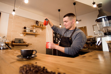 Handsome barista preparing cup of coffee for customer in coffee shop.