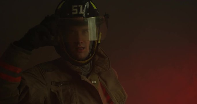 fire fighter turns to face camera and lifts up helmet visor - concerned look on face