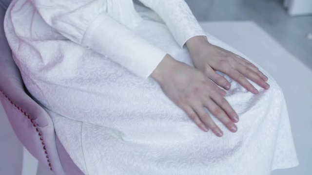 Close-up of a girl stroking her white dress . Women's hands stroking the white dress, sitting on a chair, slow motion 1920x1080