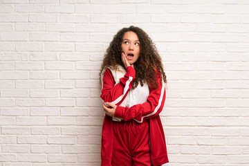 Teenager sport girl with curly hair surprised and shocked while looking right