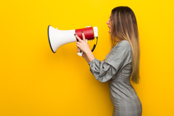 Young woman with glasses over yellow wall shouting through a megaphone to announce something in lateral position