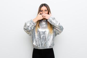 Young woman with glasses over white wall covering mouth with hands for saying something inappropriate