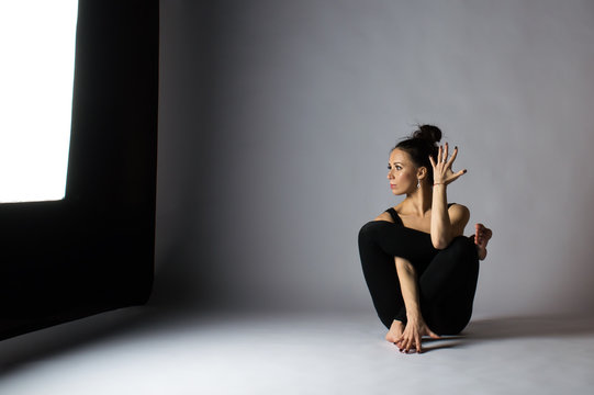 Beautiful young dark-haired girl in a black uniform and does yoga. Studio photos.