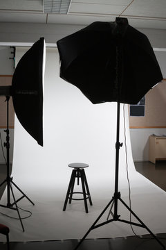 Empty photo studio with lighting equipment, white background and chair.