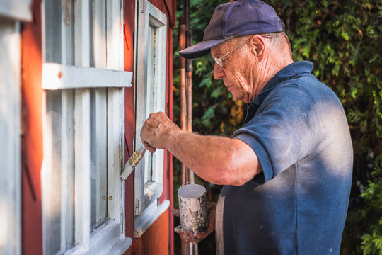Active senior man painting window frame of wooden cabin