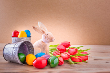 Osterhase mit Tulpen und bunten Ostereier vor einem Holz Hintergrund
