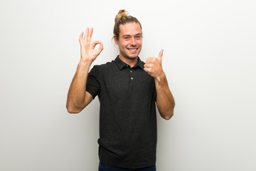Blond man with long hair over white wall showing ok sign with and giving a thumb up gesture