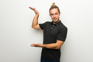 Blond man with long hair over white wall holding copyspace to insert an ad