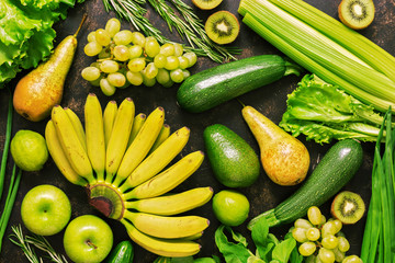 Assorted fresh vegetables and fruits of green, yellow color on a dark background. Top view, flat lay.