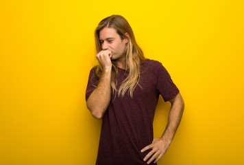 Blond man with long hair over yellow wall having doubts