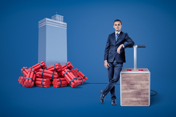 Businessman standing next to detonator box connected to heap of dynamite beside high-rise building...