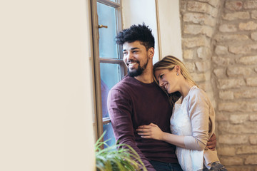 Portrait of a young couple hugging next to the window, brick wall background.