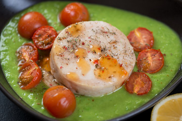 Close-up of hake medallions with green peas puree and cherry tomatoes, selective focus