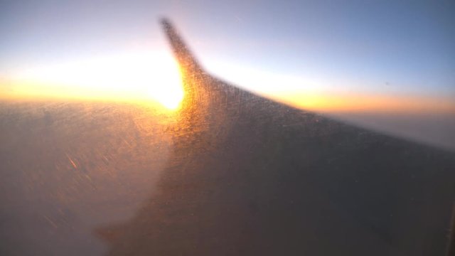 Blur view from airplane window to sunrise or sunset. Silhouette of wing of plane flying above the clouds with sun light. Aircraft flight at sky. Concept of traveling by air. Defocus shot