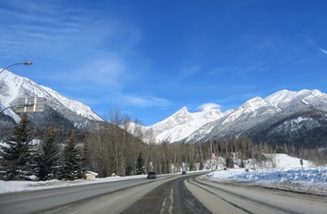 The view through the front of a car driving down the highway through the Rocky Mountains on a sunny, beautiful day outside of Fernie, British Columbia, Canada