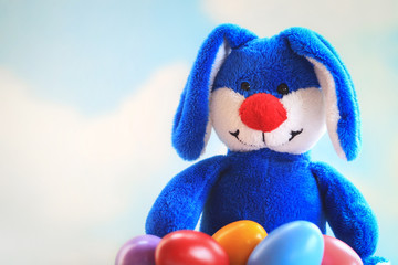 Cute blue bunny holding a bunch of colored easter eggs in his lap