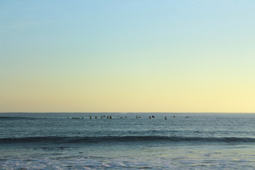 Fototapeta premium Group of surfers surfing on the blue water with sunset sky