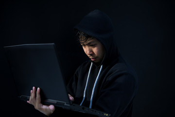 Asian hacker in black hood on black background,Hack password,hacking safety systems to steal information