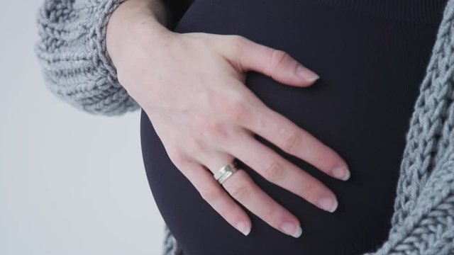A pregnant girl in a gray jacket and black lingerie stroking and hugging a big belly. 40 weeks pregnant. Belly close-up. Expecting a baby. Slow motion. 4K
