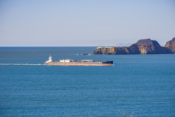 Cargo ship preparing to enter San Francisco bay; in the background Point Bonita Lighthouse, California