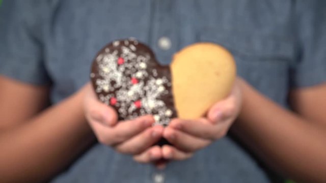 Closeup front view of cute small hands of young kid holding special sweet cookie in shape of heart. Happy Valentine day oy Mothres day holiday celebration concept. Real time 4k video footage.