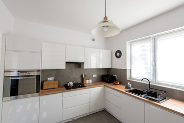 Minimal white kitchen interior with wooden countertop. Real photo