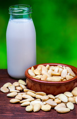 Almond milk in glass bottle. Includes peeled almonds. On green natural background.