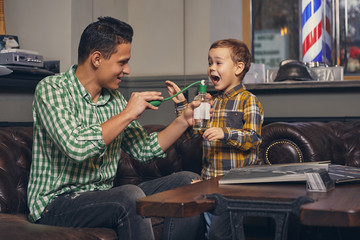 Young father and his stylish little son in the barbershop in the waiting room.