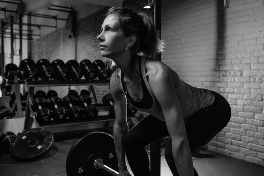 young sporty woman doing deadlift indoors in a gym with the barbell