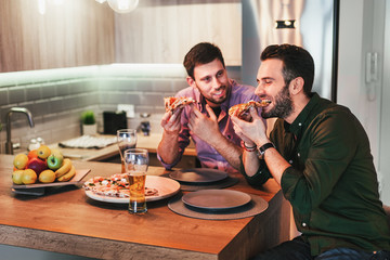 Two guys eating pizza and drinking beer at home