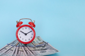 The alarm clock stands on a stack of money on a blue background