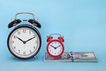 The alarm clock stands on a stack of money on a blue background