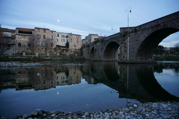 Obraz premium mirror reflection of an old stone bridge and waterfront by the river at dusk with the full moon in France 
